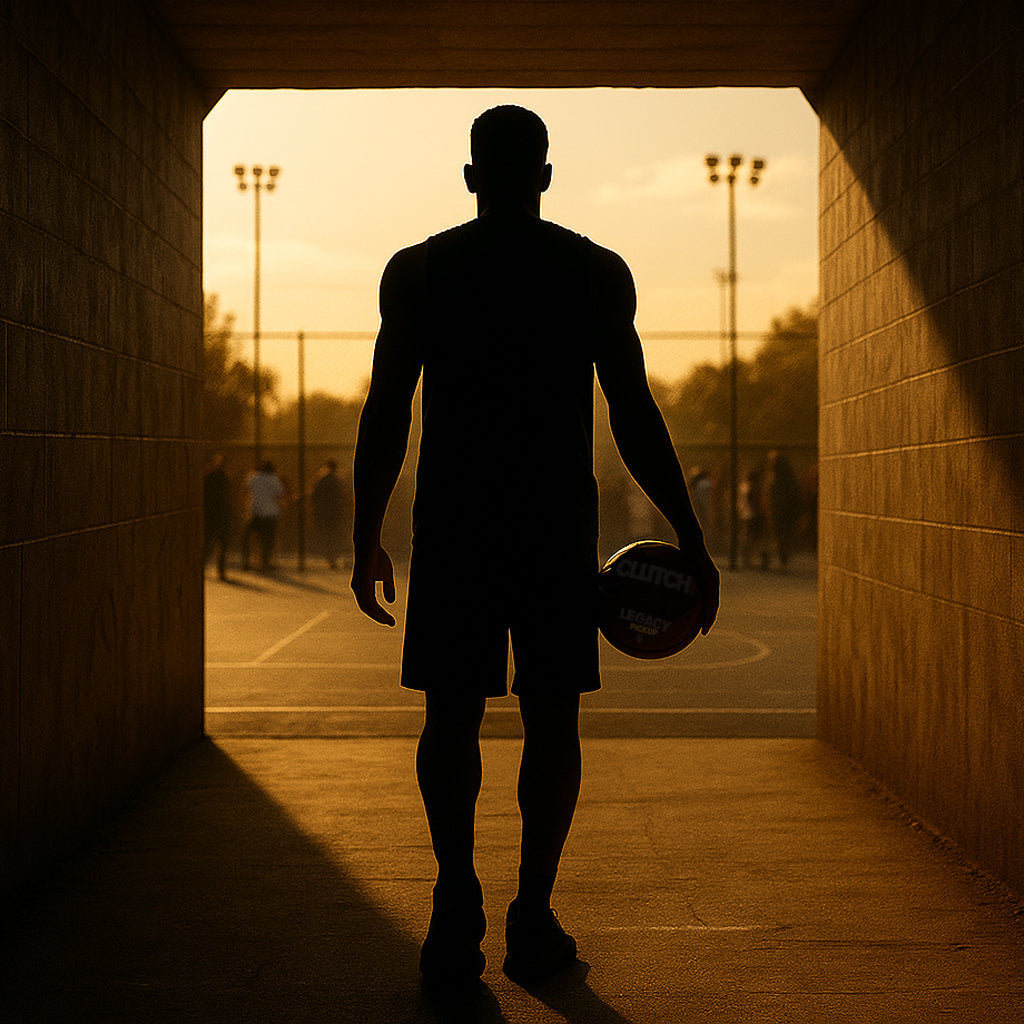 Silhouette of a person holding a basketball walking out of a tunnel onto a basketball court.
